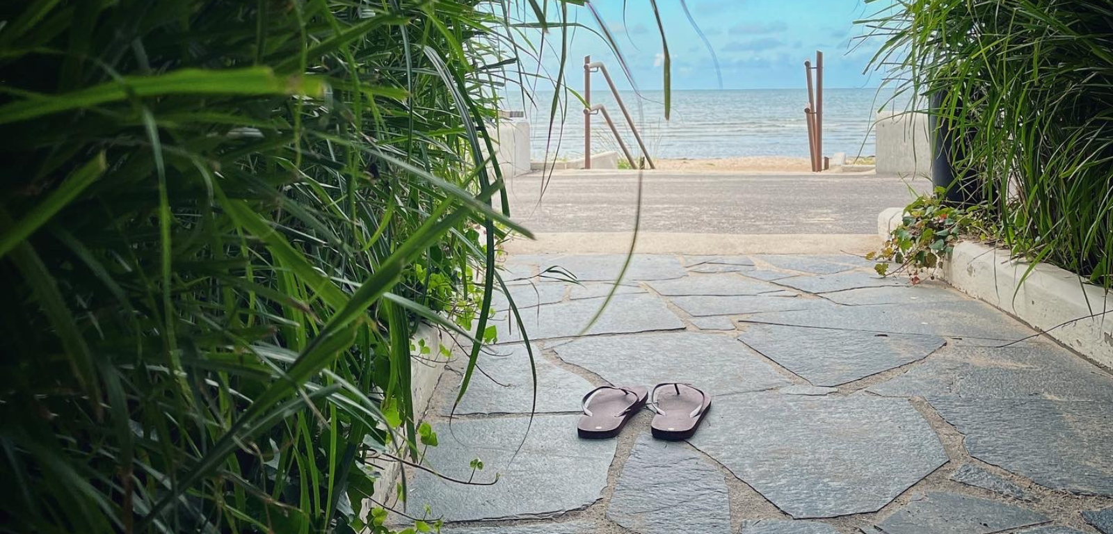 Hav i bakgrunden och ett par flipp-flopp sandaler som står på en stengång